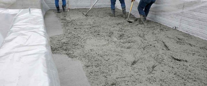 Three workers using tools to smooth freshly poured concrete on a construction site.