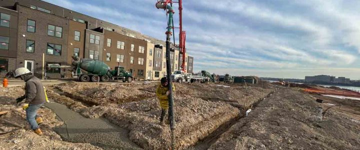 Construction workers using a concrete pump to pour concrete into forms at a large-scale building project.