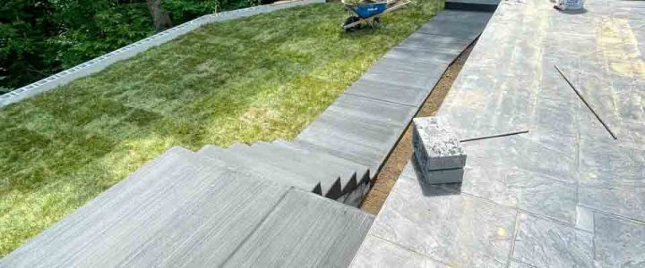 A completed concrete patio and walkway featuring a clean, polished finish and surrounding landscaping.